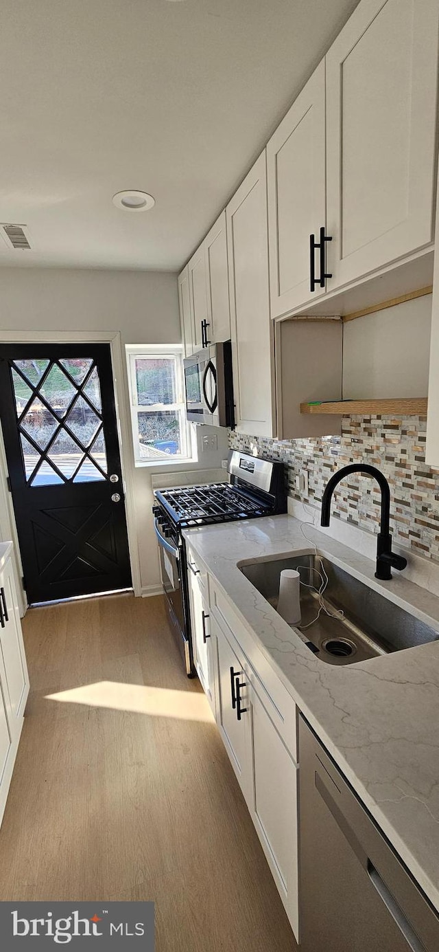 kitchen with sink, white cabinets, stainless steel appliances, light stone countertops, and light hardwood / wood-style flooring