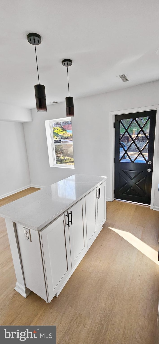 interior space with light hardwood / wood-style flooring, light stone countertops, hanging light fixtures, and white cabinets