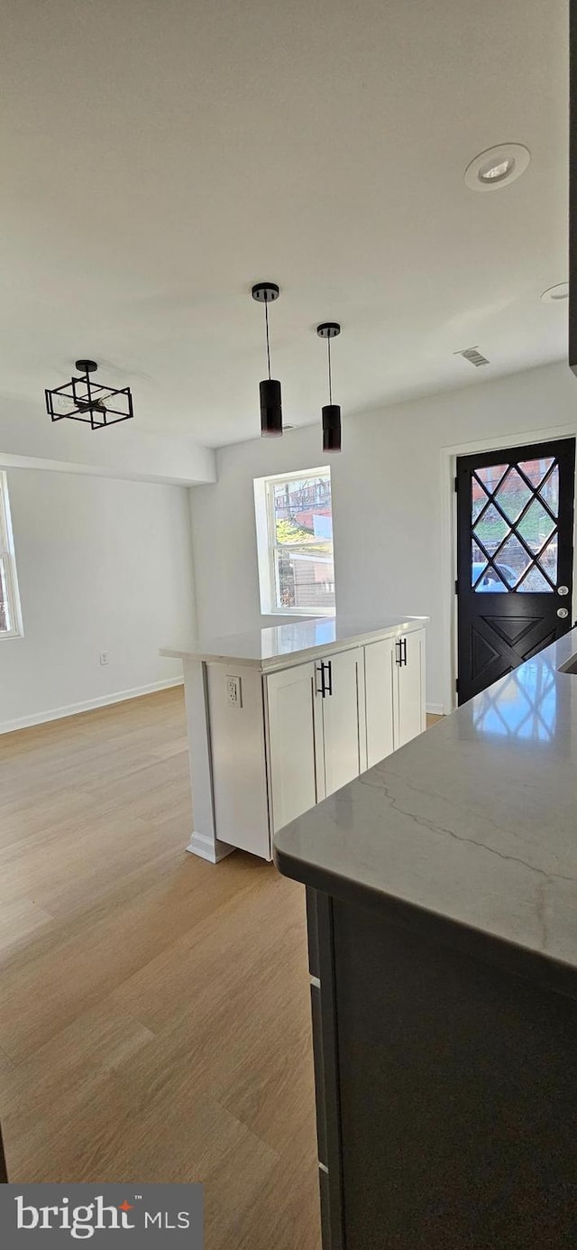 kitchen with decorative light fixtures, light stone countertops, light wood-type flooring, and white cabinets