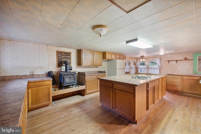 kitchen featuring a center island, a wood stove, white refrigerator, light wood-type flooring, and stainless steel gas stovetop