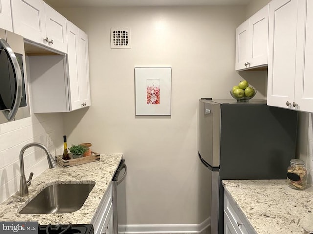 kitchen featuring visible vents, white cabinets, light stone counters, a sink, and backsplash