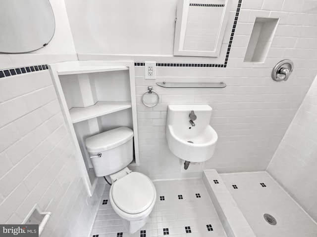 bathroom with tiled shower, toilet, tile patterned flooring, and tile walls