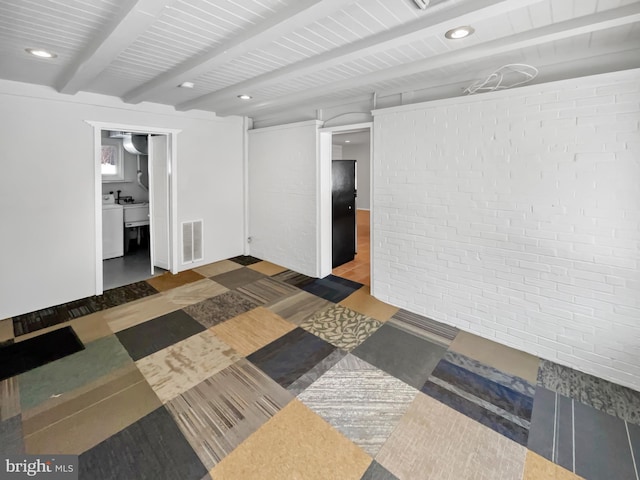 spare room featuring washer / clothes dryer, beam ceiling, and brick wall