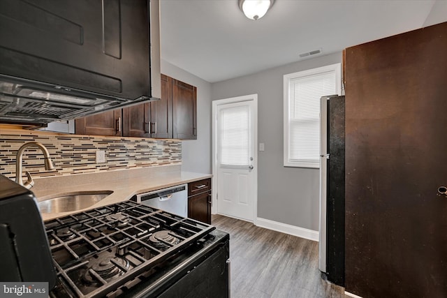 kitchen with sink, wood-type flooring, dark brown cabinets, stainless steel appliances, and backsplash