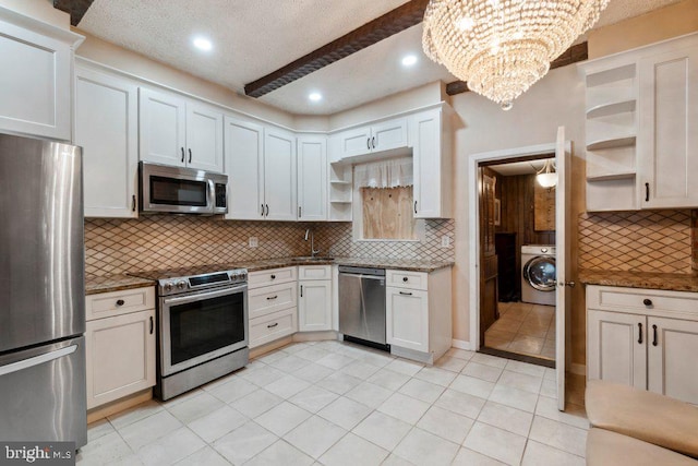 kitchen with dark stone countertops, backsplash, stainless steel appliances, white cabinets, and washer / dryer