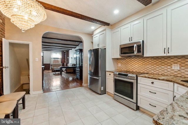 kitchen with white cabinets, stainless steel appliances, beam ceiling, light stone countertops, and backsplash