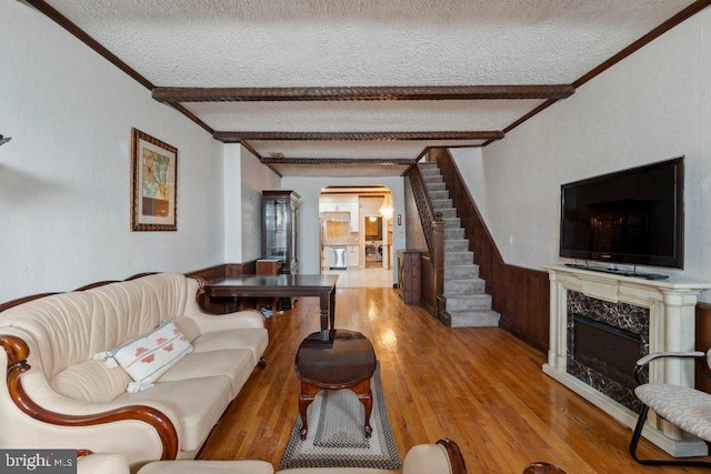 living room featuring beam ceiling, ornamental molding, a high end fireplace, light hardwood / wood-style floors, and a textured ceiling