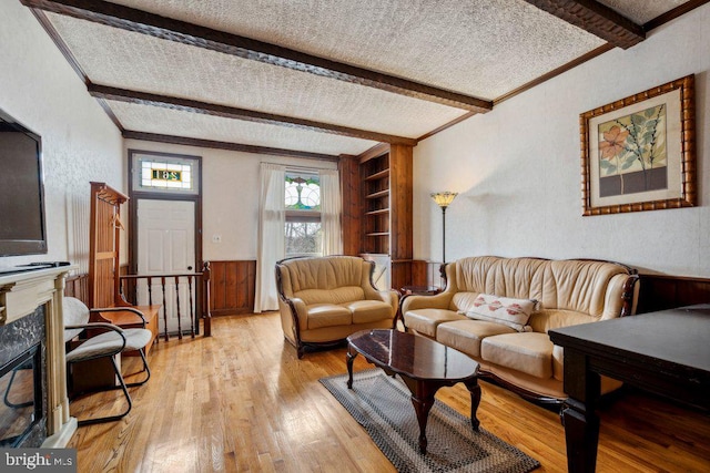 living room featuring a textured ceiling, a fireplace, light hardwood / wood-style floors, and beamed ceiling