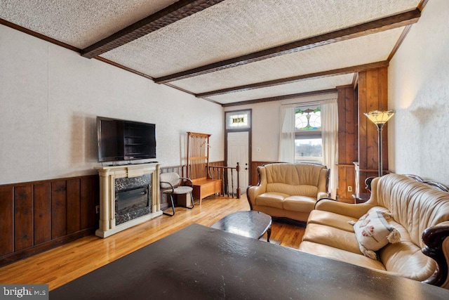 living room with beam ceiling, light hardwood / wood-style flooring, ornamental molding, and wooden walls