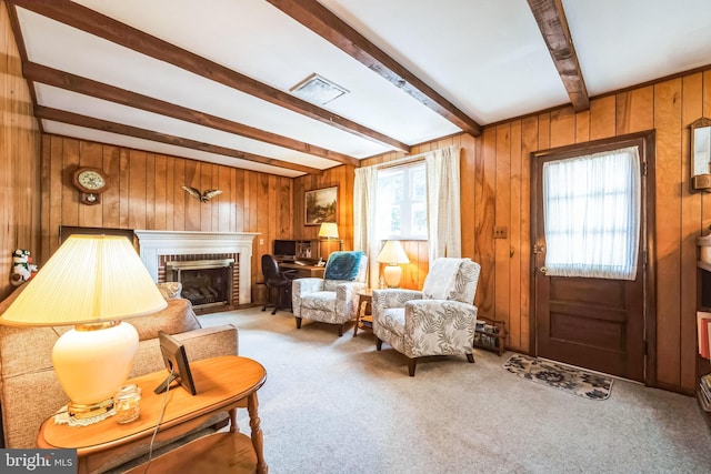 sitting room with a brick fireplace, beam ceiling, wooden walls, and carpet