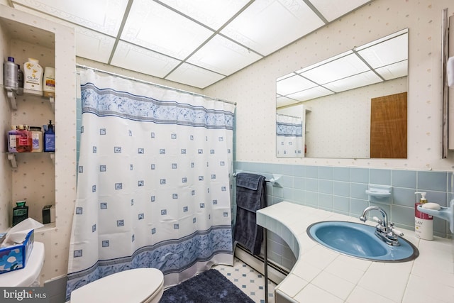 bathroom with toilet, curtained shower, sink, and tile walls