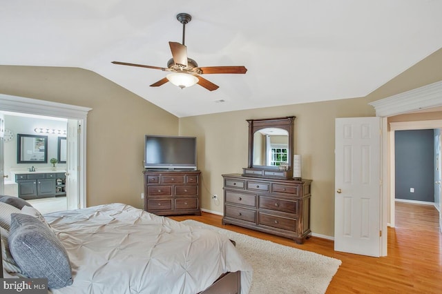 bedroom featuring ceiling fan, ensuite bath, lofted ceiling, and light wood-type flooring