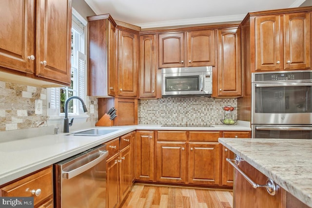 kitchen with tasteful backsplash, sink, ornamental molding, stainless steel appliances, and light wood-type flooring