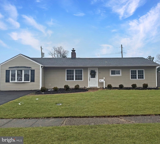 ranch-style home with a front lawn, roof with shingles, driveway, and a chimney