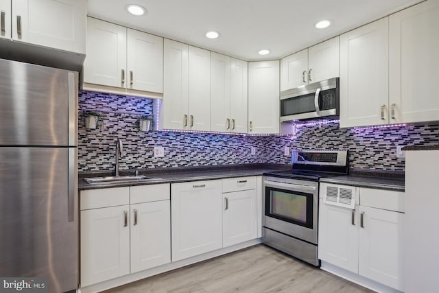 kitchen with light wood finished floors, a sink, stainless steel appliances, white cabinetry, and dark countertops