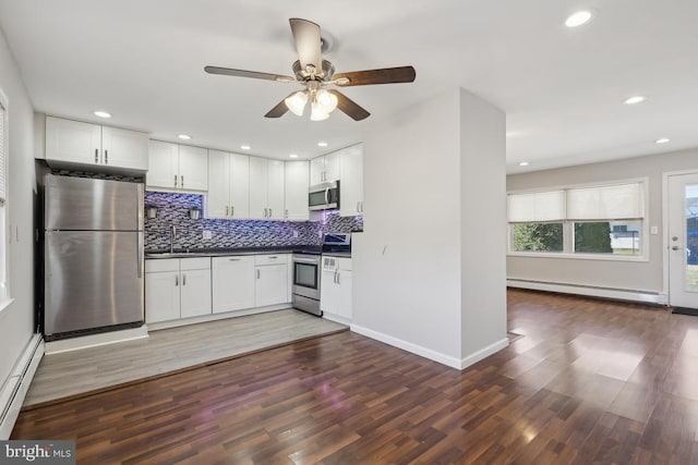 kitchen with a sink, dark countertops, baseboard heating, and stainless steel appliances