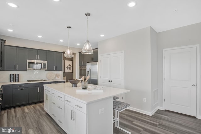 kitchen featuring pendant lighting, appliances with stainless steel finishes, gray cabinetry, a center island, and a kitchen bar