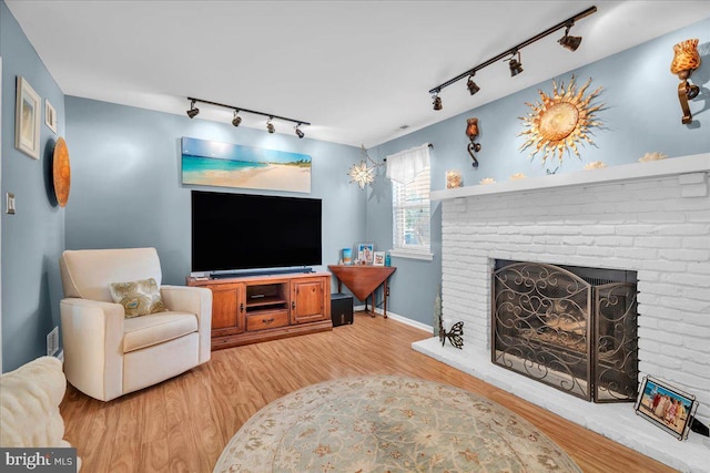 living room featuring wood-type flooring, rail lighting, and a brick fireplace