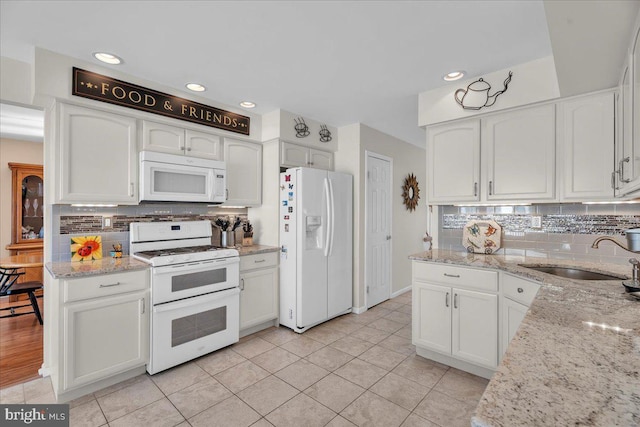 kitchen featuring sink, white cabinetry, white appliances, light stone countertops, and decorative backsplash