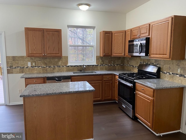 kitchen with sink, stainless steel appliances, dark hardwood / wood-style floors, light stone counters, and a kitchen island