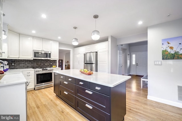 kitchen with hanging light fixtures, appliances with stainless steel finishes, a kitchen island, decorative backsplash, and white cabinets