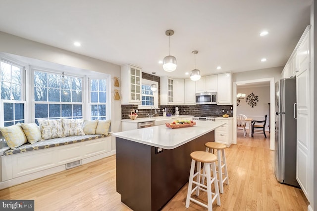 kitchen featuring decorative light fixtures, white cabinetry, a center island, light hardwood / wood-style floors, and stainless steel appliances