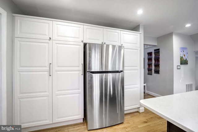 kitchen featuring stainless steel fridge, light hardwood / wood-style floors, and white cabinets