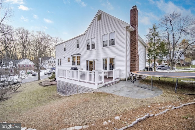 back of house featuring a trampoline, a wooden deck, a lawn, and a patio