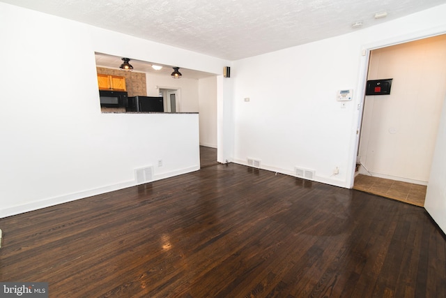 unfurnished living room with a textured ceiling, wood finished floors, visible vents, and baseboards