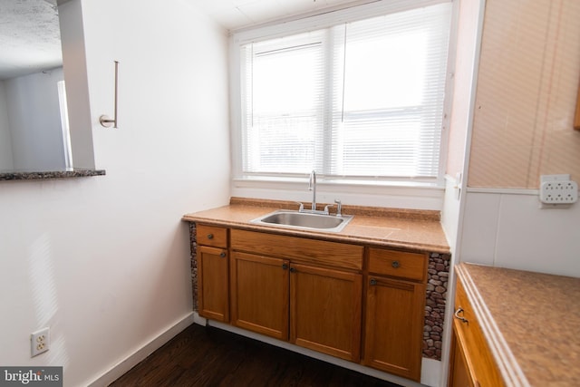 kitchen with brown cabinets, dark wood-type flooring, light countertops, and a sink