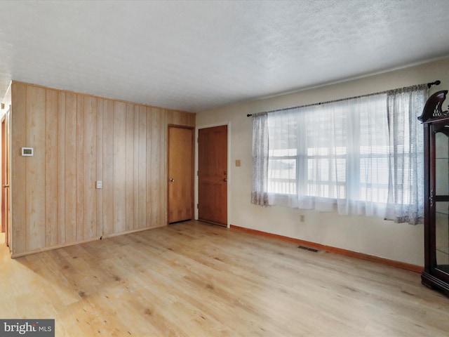 empty room featuring wood walls, a textured ceiling, and light hardwood / wood-style flooring