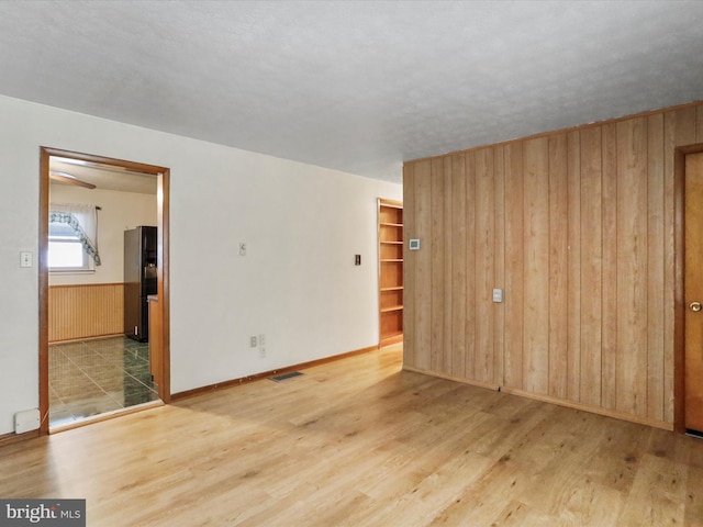 spare room with built in shelves, light hardwood / wood-style floors, and wood walls