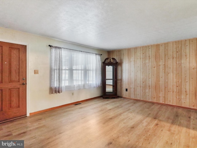 interior space with wooden walls, a textured ceiling, and light wood-type flooring