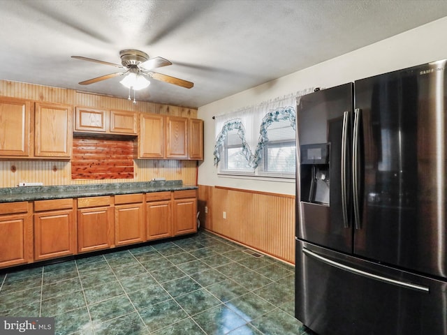 kitchen featuring stainless steel refrigerator with ice dispenser, ceiling fan, a textured ceiling, and wood walls