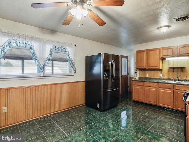 kitchen featuring sink, refrigerator with ice dispenser, a textured ceiling, and wood walls