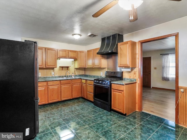 kitchen with sink, stainless steel refrigerator, ceiling fan, black range with gas stovetop, and wall chimney exhaust hood