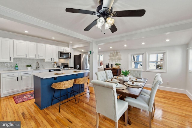 dining area featuring sink, ornamental molding, ceiling fan, and light wood-type flooring