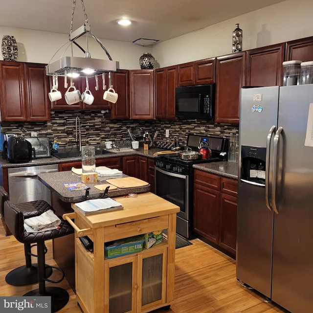 kitchen with tasteful backsplash, sink, a kitchen breakfast bar, stainless steel appliances, and light wood-type flooring