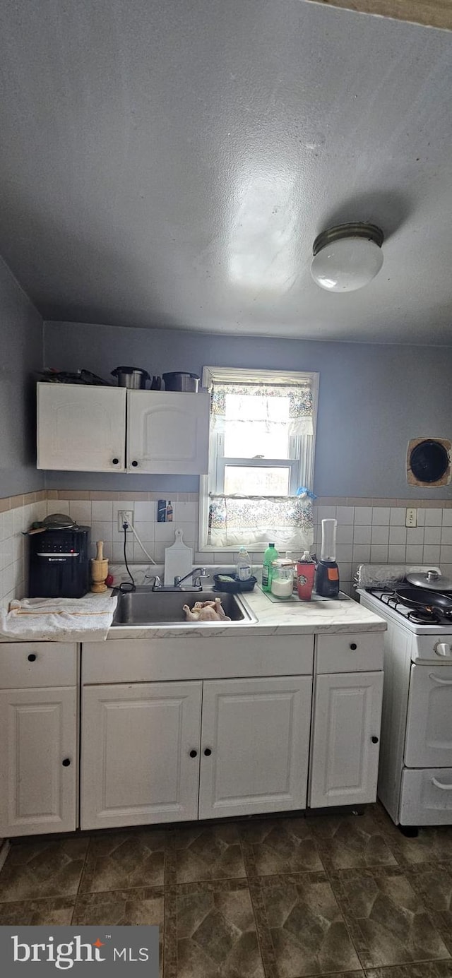 kitchen with white cabinetry, sink, decorative backsplash, and white gas range oven