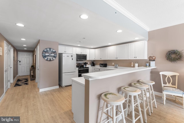 kitchen with range with electric stovetop, a kitchen breakfast bar, kitchen peninsula, white fridge, and white cabinets