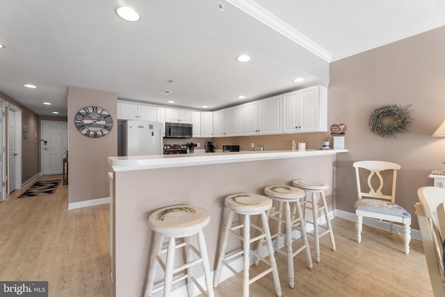 kitchen featuring white cabinetry, a kitchen bar, white fridge, light hardwood / wood-style floors, and kitchen peninsula