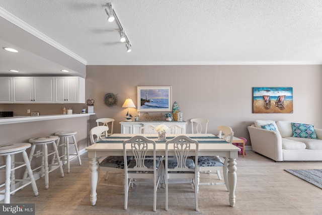 dining area featuring ornamental molding, rail lighting, a textured ceiling, and light wood-type flooring