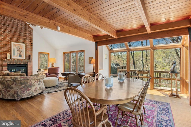 dining space featuring vaulted ceiling with beams, wooden ceiling, wood finished floors, and a fireplace