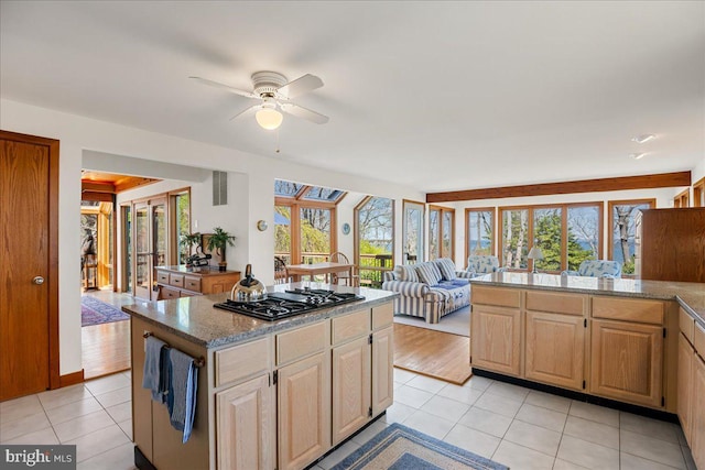 kitchen with ceiling fan, light tile patterned floors, a kitchen island, and black gas stovetop