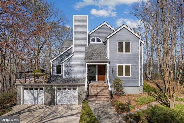 traditional-style home featuring a shingled roof, a chimney, an attached garage, and driveway