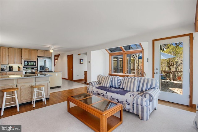 living room featuring baseboards, a ceiling fan, and light wood-style flooring