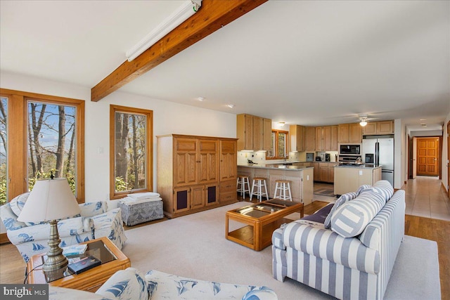 living area with a ceiling fan and beamed ceiling