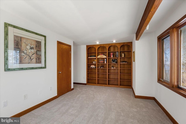 carpeted spare room with baseboards, built in shelves, and beamed ceiling