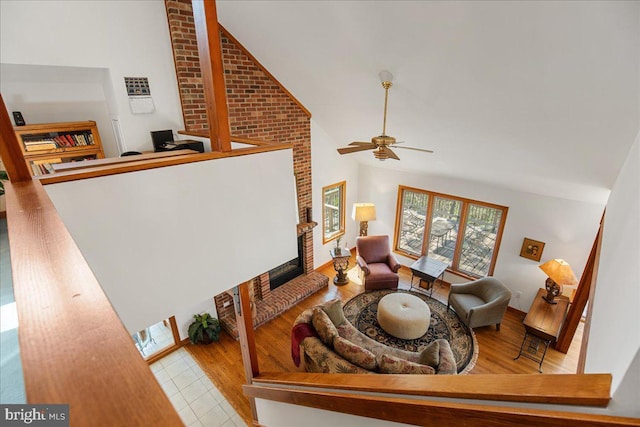 living area with high vaulted ceiling, a ceiling fan, a brick fireplace, and wood finished floors