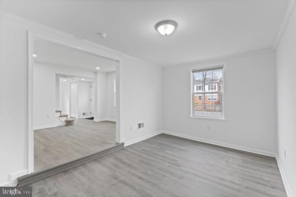 empty room with crown molding and light hardwood / wood-style floors